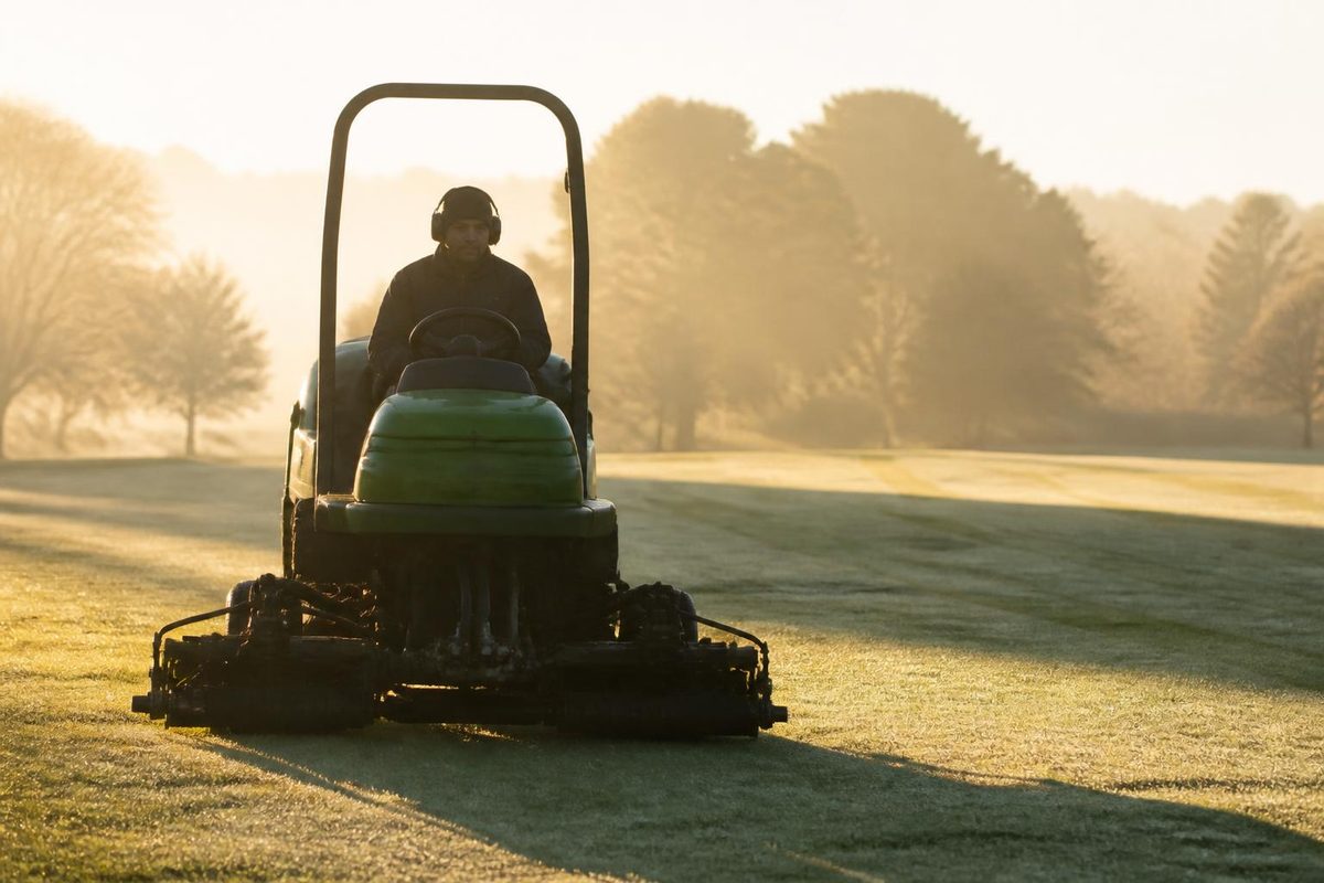 Greenkeeper cutting a golf fairway at dawn